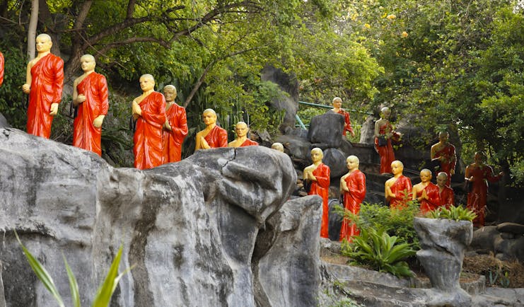 Monk statues, dressed in orange, lining the hillside at the Golden Temple in the Cultural Triangle