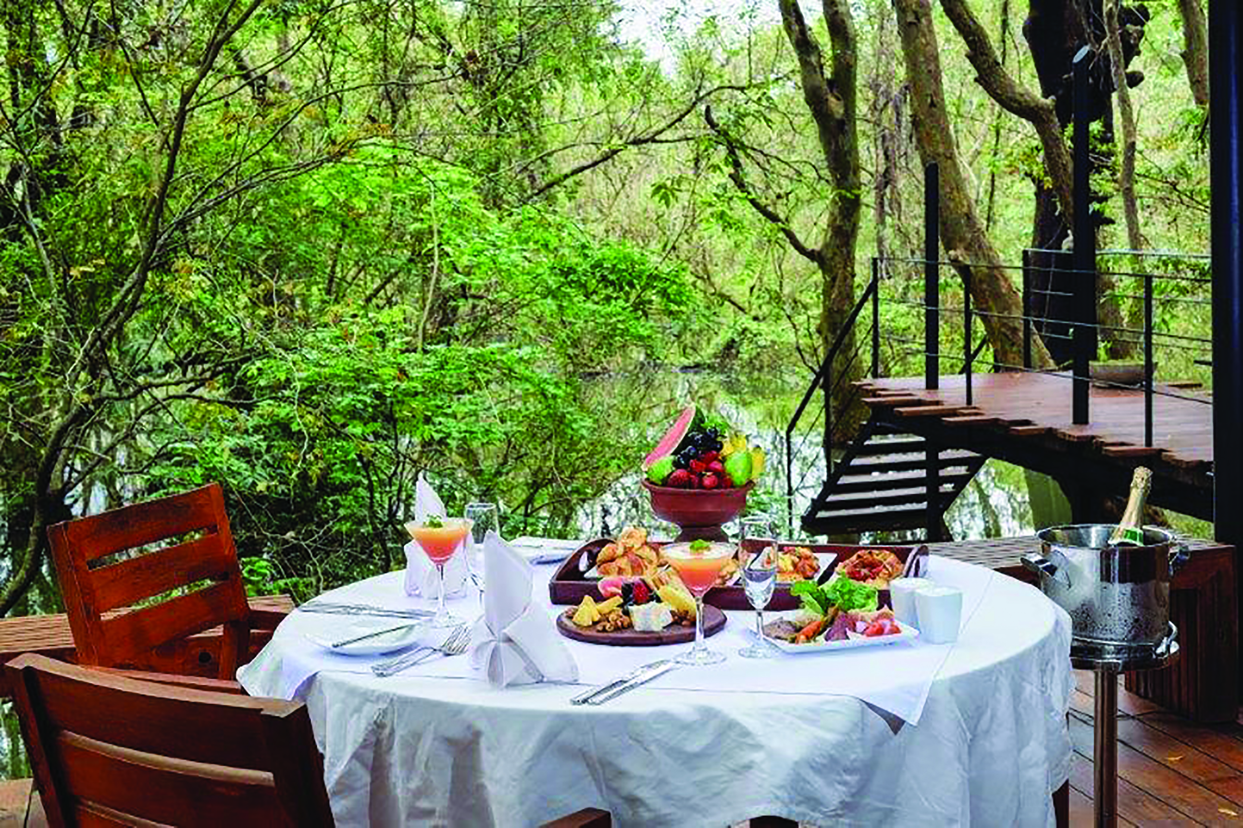 Kalundewa Retreat table on terrace set ofr breakfast with pastries and fresh fruit, views over lake and tree tops