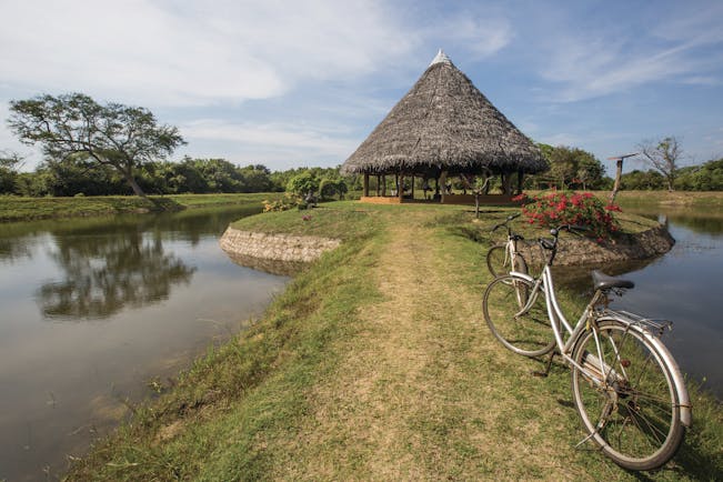 The Mudhouse yoga pavilion, bicycles, hut on grass mound surrounded by water