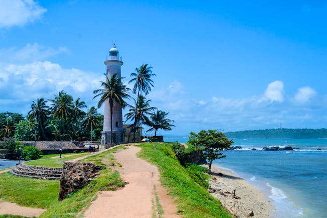 Lighthouse overlooking sea in Galle, palm trees, beach