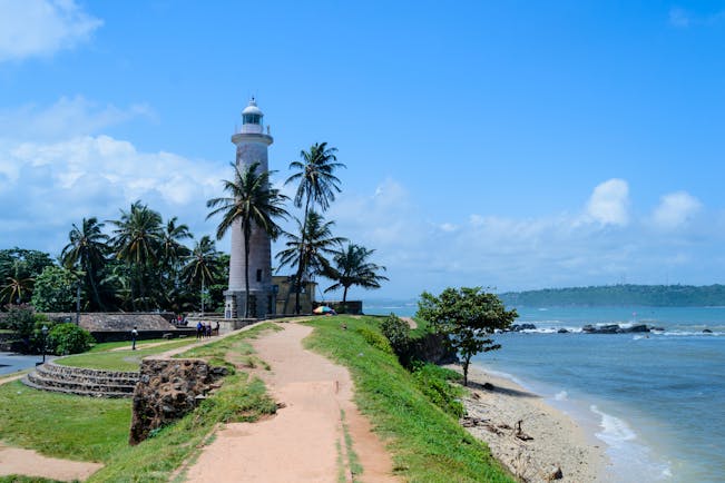 Lighthouse overlooking sea in Galle, palm trees, beach