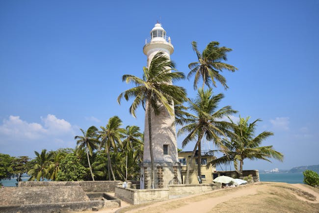 Lighthouse on beach in Dondra, white building, palm trees, sand