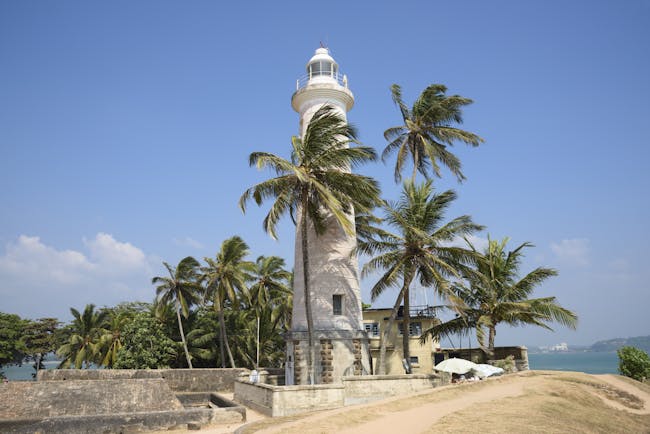 Lighthouse on beach in Dondra, white building, palm trees, sand
