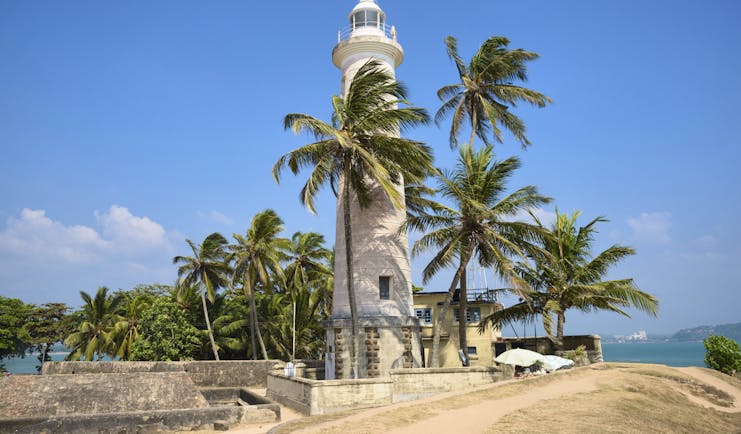 Lighthouse on beach in Dondra, white building, palm trees, sand