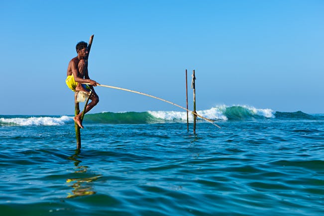 A stilt fisherman sitting on stilts in the sea, fishing for fish