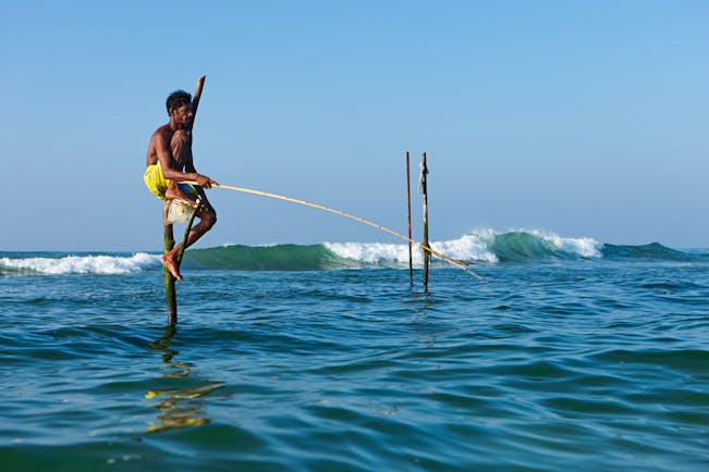 A stilt fisherman sitting on stilts in the sea, fishing for fish
