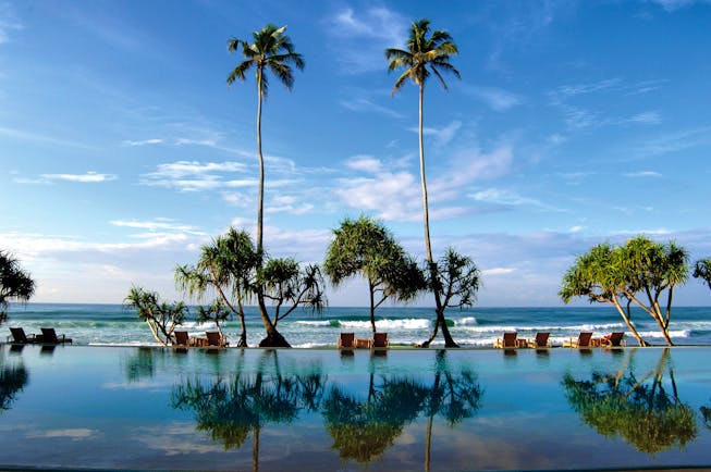 Outdoor infinity pool leading onto beach with palm trees and sunloungers
