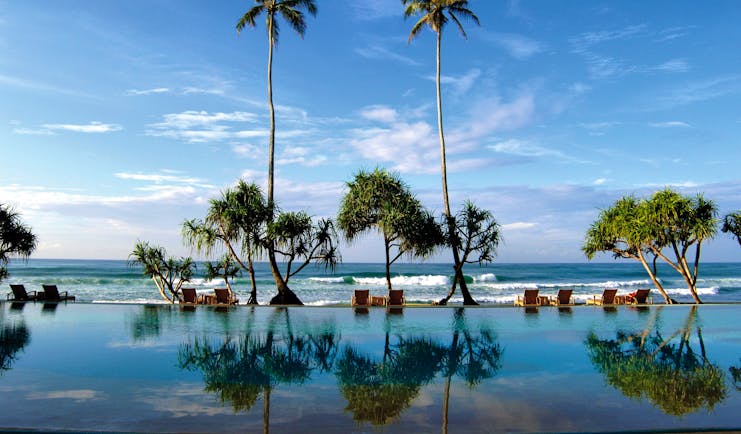 Outdoor infinity pool leading onto beach with palm trees and sunloungers