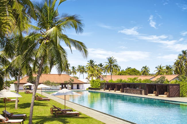 Outdoor pool with palm trees near by and sunbeds and umbrellas on grass