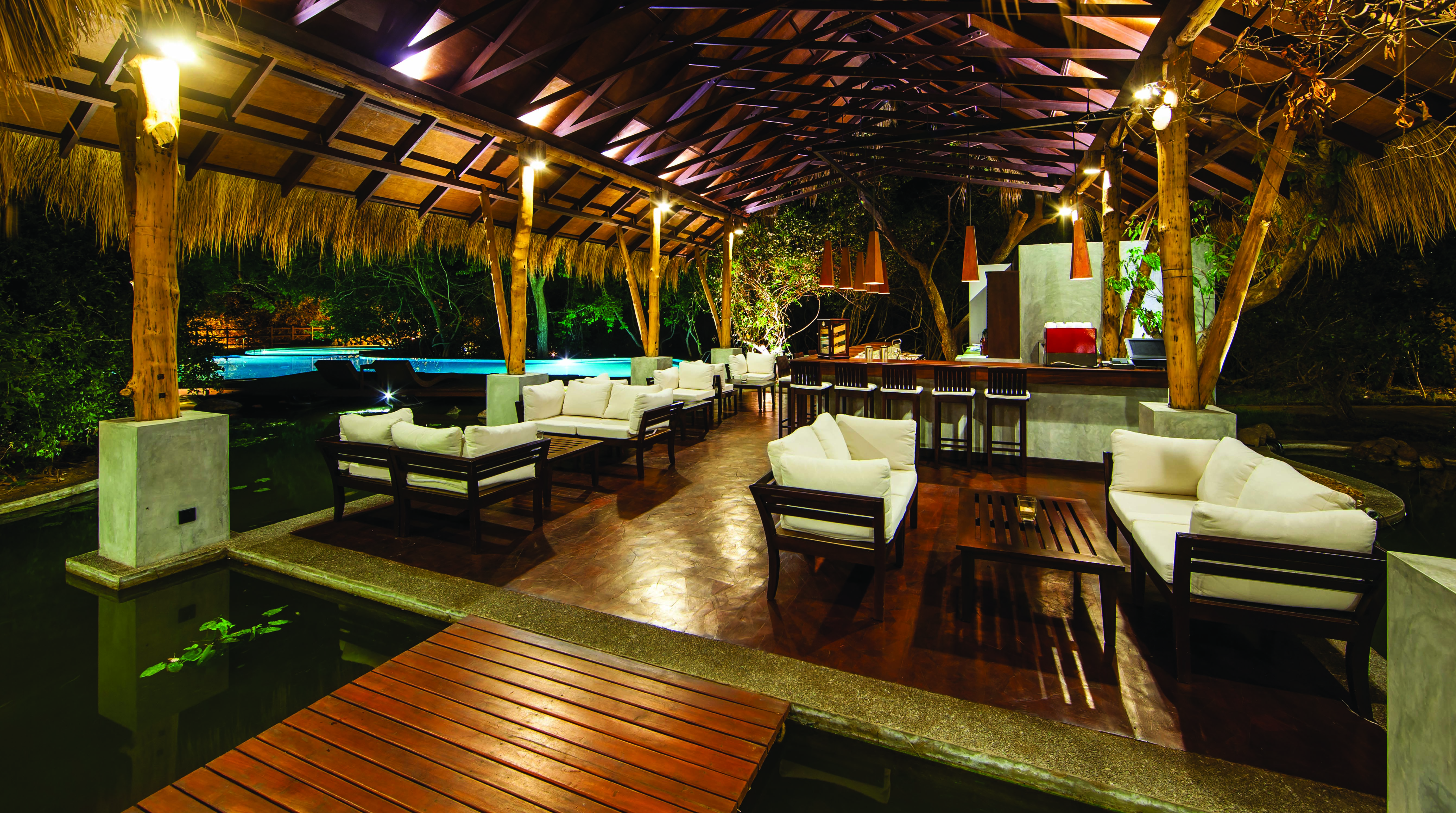 Jungle Beach bar, thatched structure beside pool with sofas and tables, soft lighting