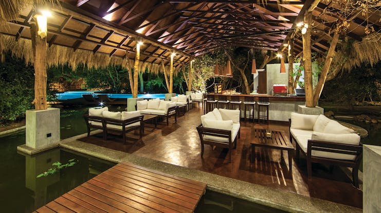 Jungle Beach bar, thatched structure beside pool with sofas and tables, soft lighting