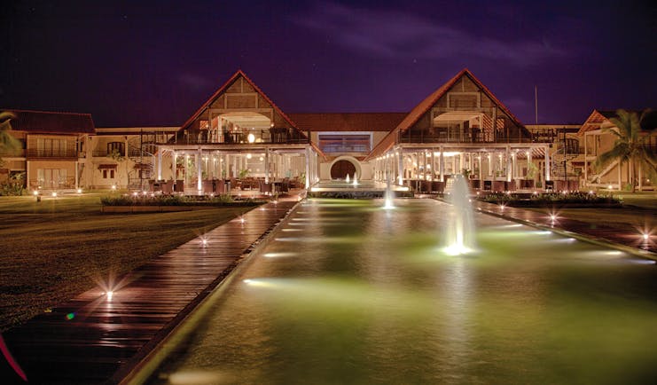 Exterior of hotel at night with fountains in front 