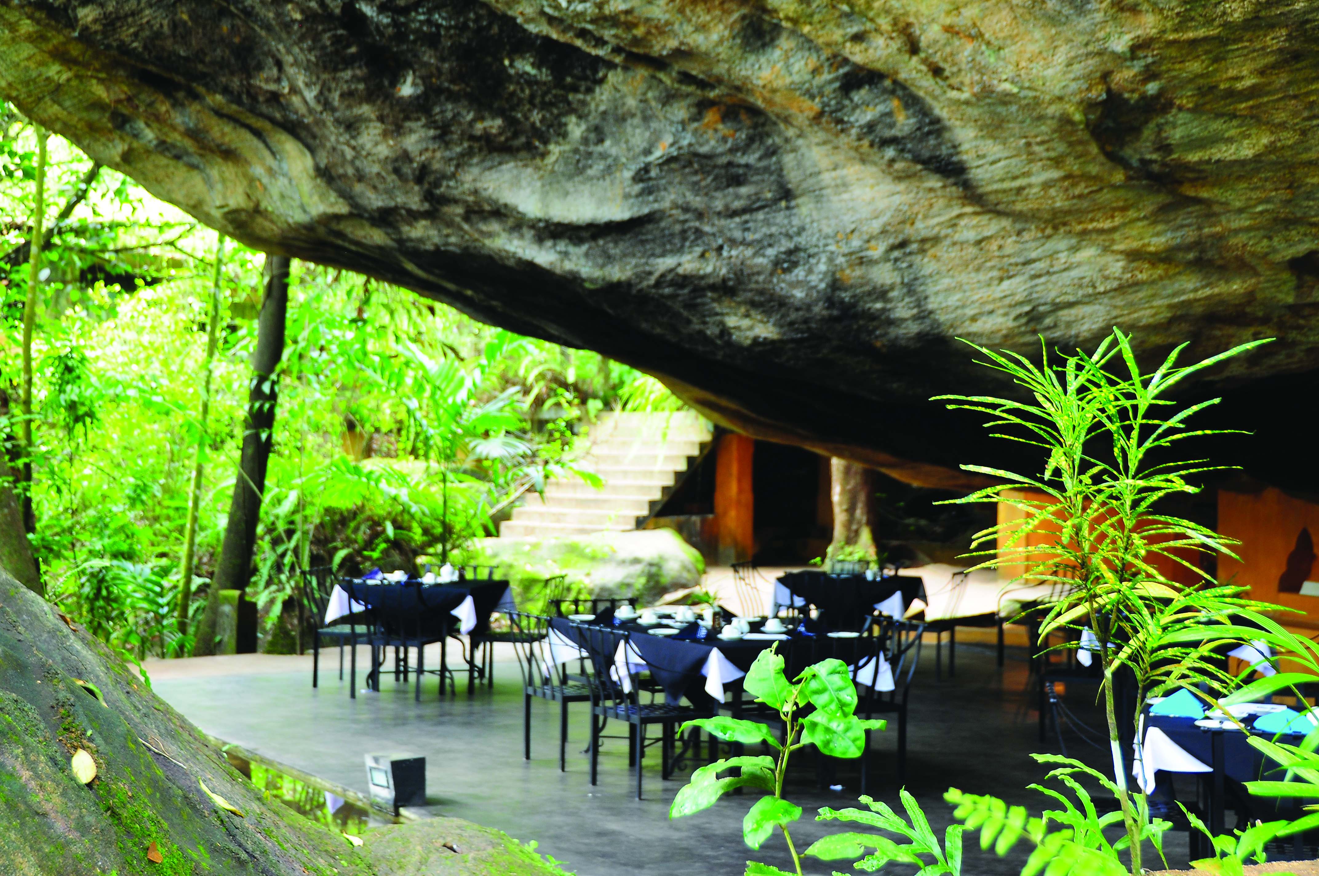 Boulder Garden restaurant outside placed underneath boulder rock formation, black tables and chairs on patio