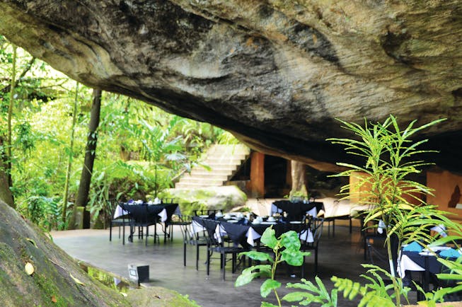 Boulder Garden restaurant outside placed underneath boulder rock formation, black tables and chairs on patio