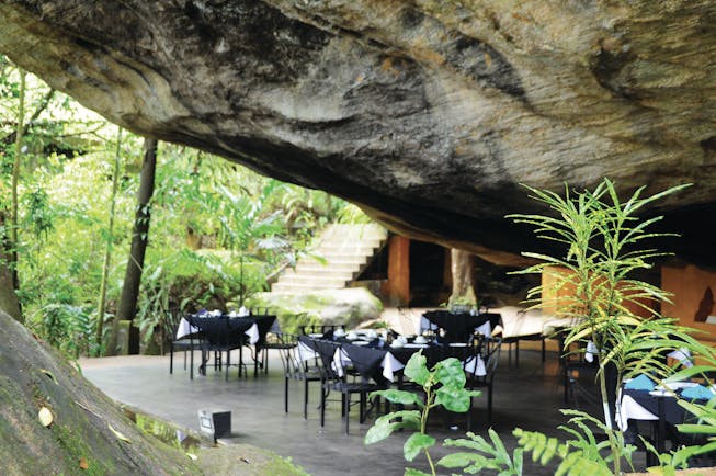 Boulder Garden restaurant outside placed underneath boulder rock formation, black tables and chairs on patio