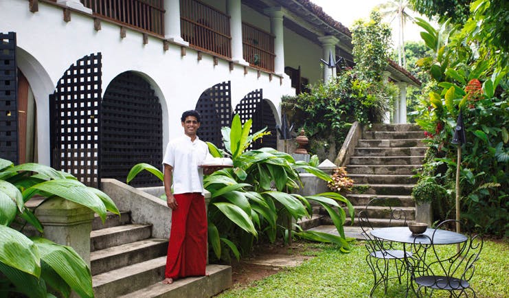 The Kandy House Sri Lanka Black Raja Suite exterior staff member with tray garden seating area
