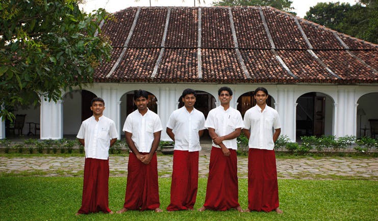 The Kandy House Sri Lanka staff members in traditional dress in front of bungalow