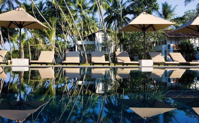 Pool view with beige sunloungers and umbrellas on the pool edge 