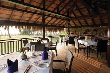 Reef Villa and Spa restaurant, tables and chairs under thatched roof, rustic building overlooking gardens