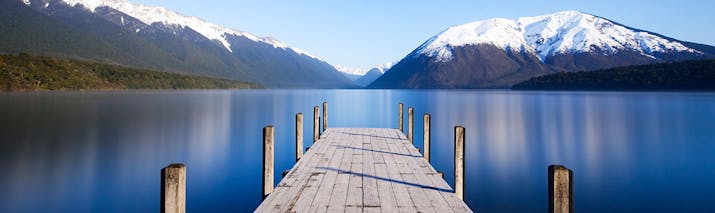 Wooden jetty into calm blue lake with snowy mountains in distance