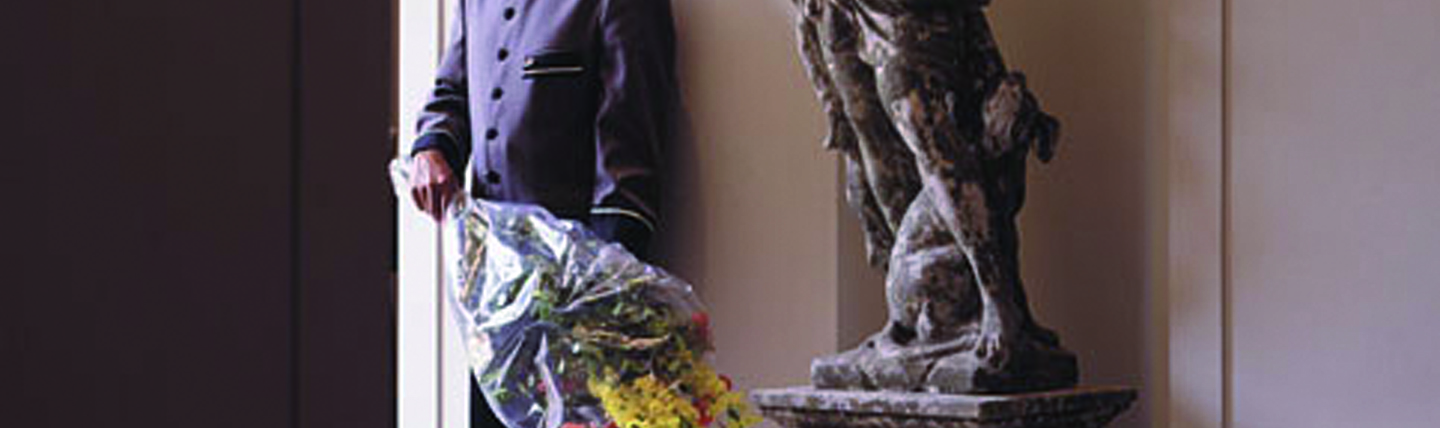 Man in hotel uniform standing next to statue with bouquet of flowers
