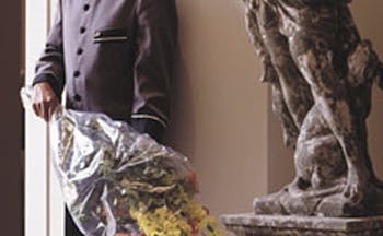 Man in hotel uniform standing next to statue with bouquet of flowers
