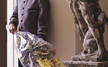 Man in hotel uniform standing next to statue with bouquet of flowers