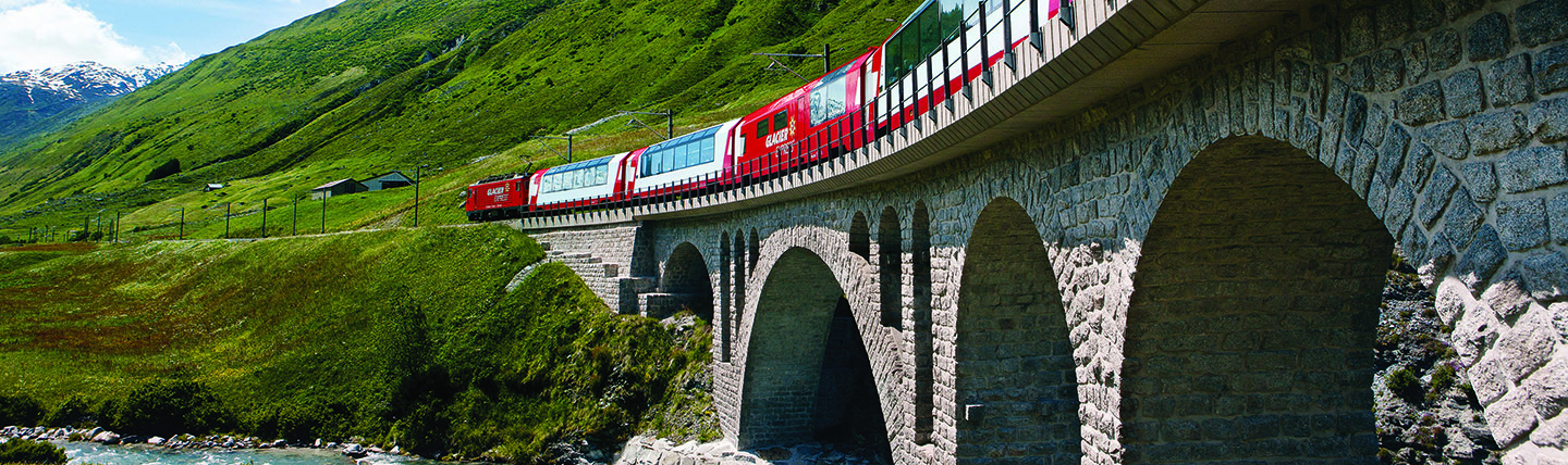 Red train with large windows on bridge in summer mountain landscape