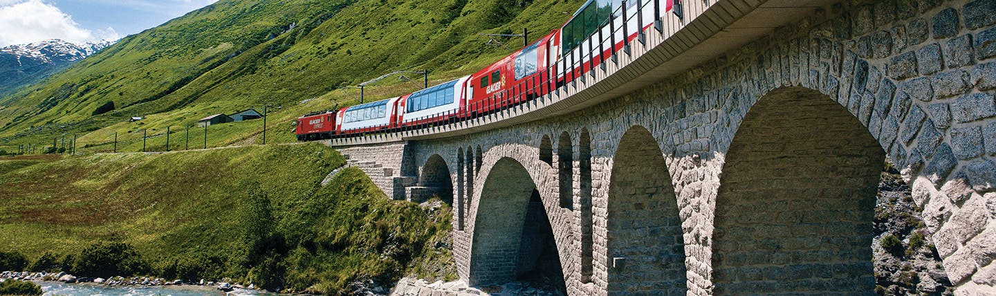 Red train with large windows on bridge in summer mountain landscape