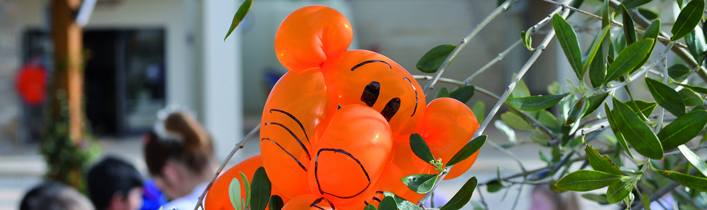 Orange plastic inflated tiger next to kids and olive tree