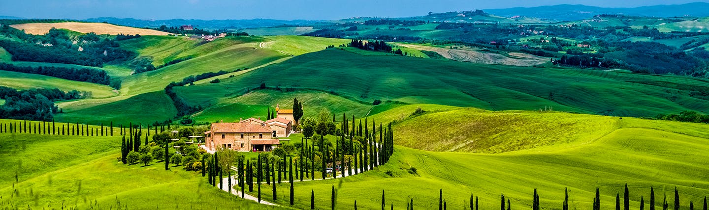 Scenic view of Tuscan landscape with green rolling fields, a farmhouse and Cypress trees