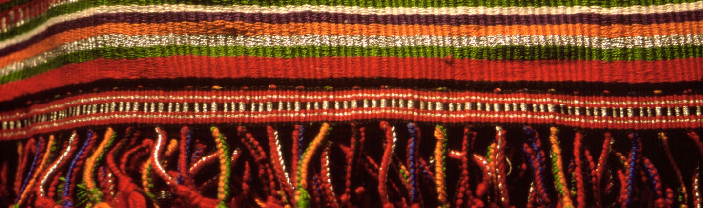 Woven mat in colours of ochre, red, orange and some green stripes