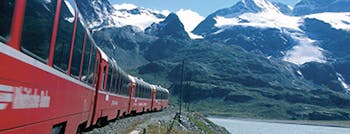 Red train with large windows with snowy mountains in background
